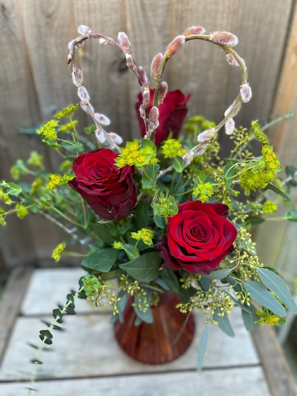 Three red roses in a red glass vase