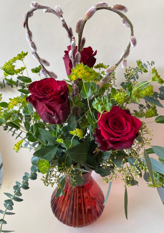 Three red roses in a red glass vase