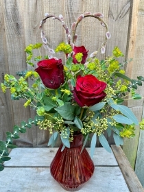 Three red roses in a red glass vase